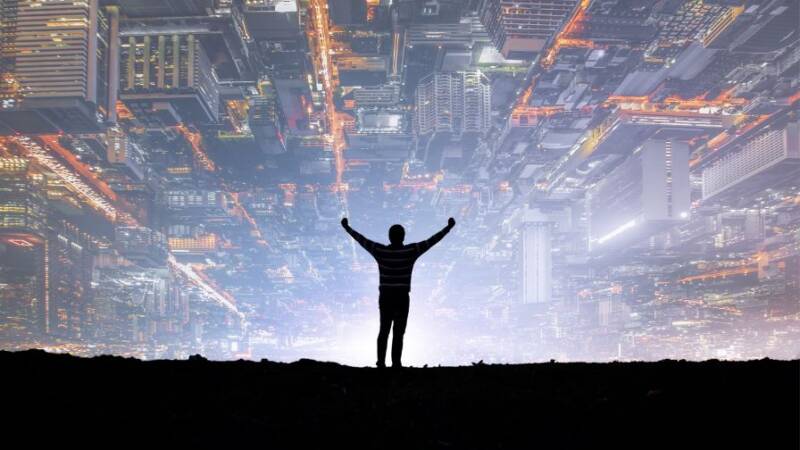Silhouette of man standing with arms raised with top-down view of buildings in the sky
