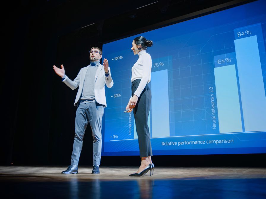 Two people presenting on stage with a data graph projected behind them