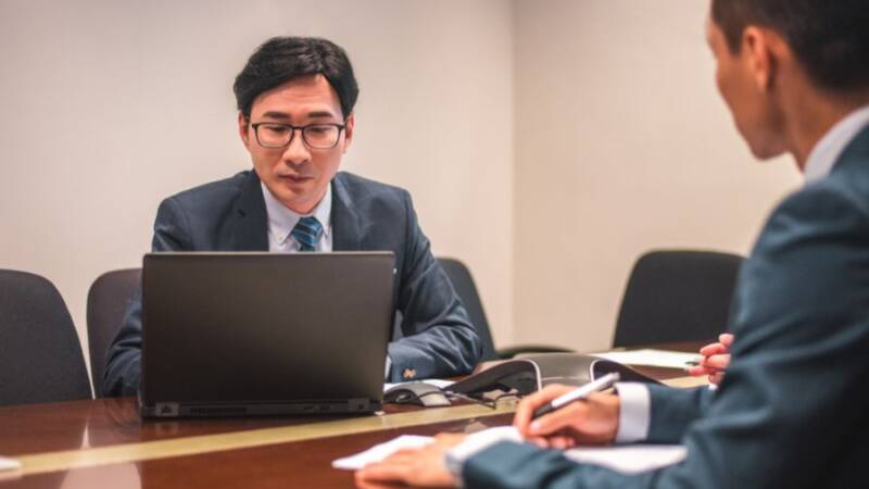 Two businessmen sitting at a desk work on a laptop