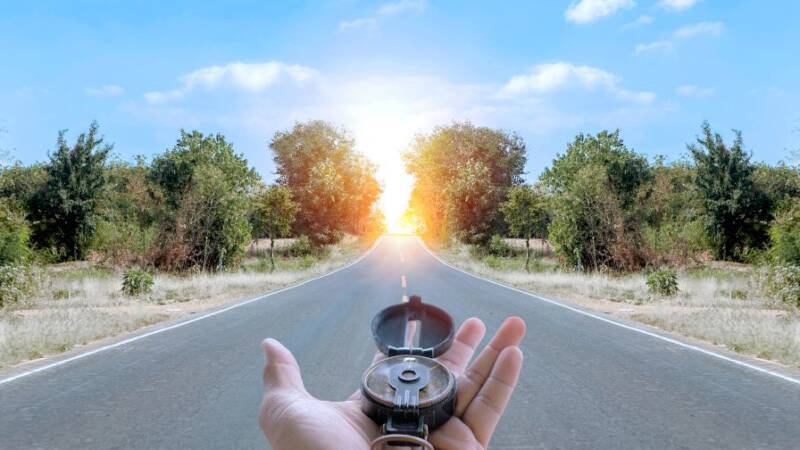 Hand holding compass on highway to sunset