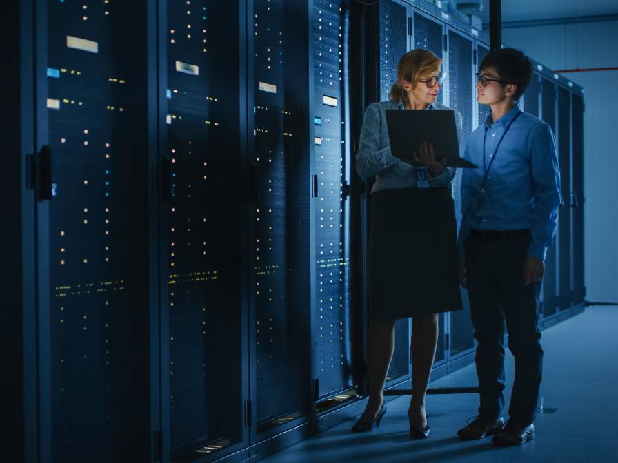 Two office workers on the computer standing outside of a server room