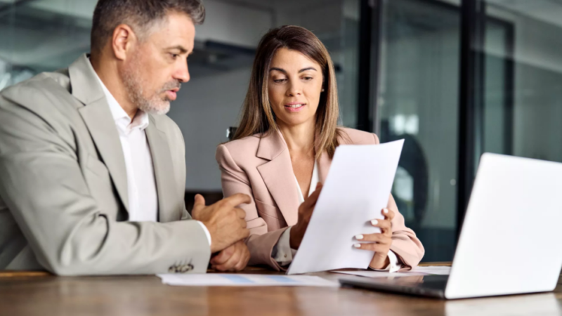 Woman showing man research at desk in office