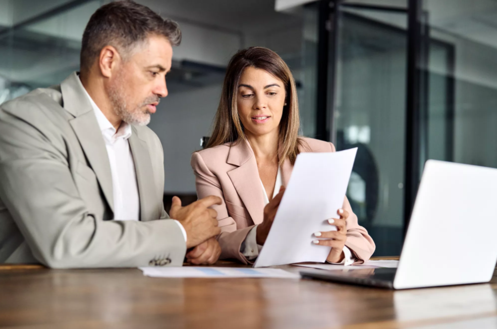 Woman showing man research at desk in office